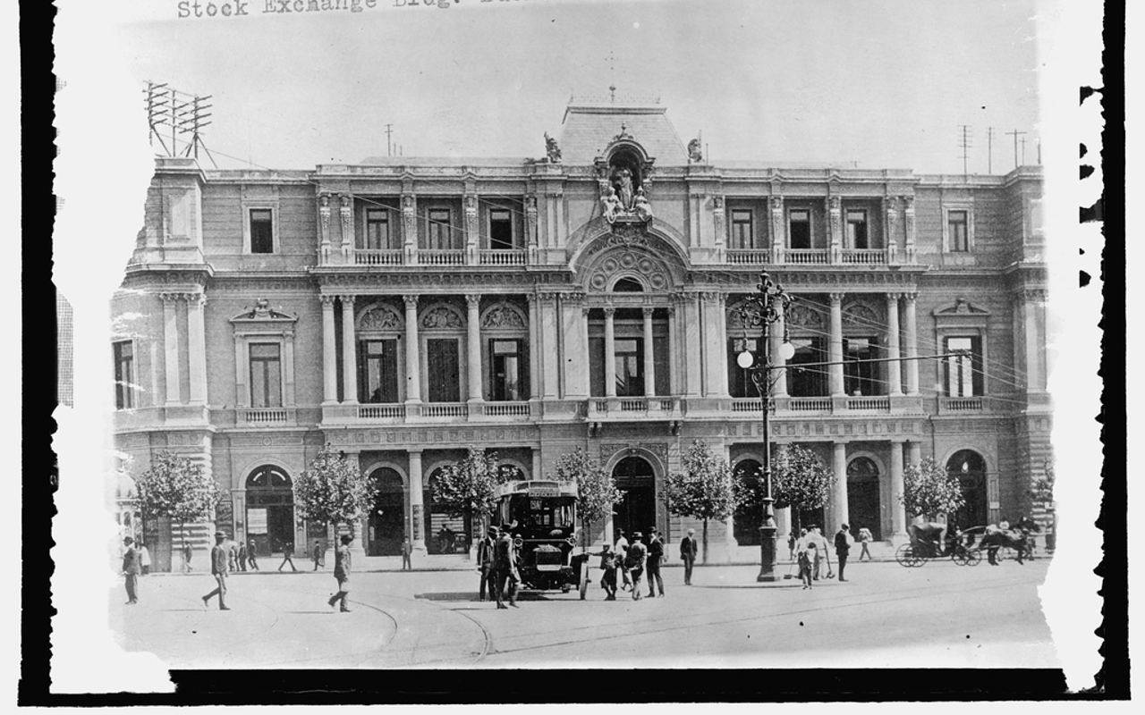 Fotografía histórica de la fachada de la Bolsa de Comercio de Buenos Aires, con peatones y carruajes en la calle.