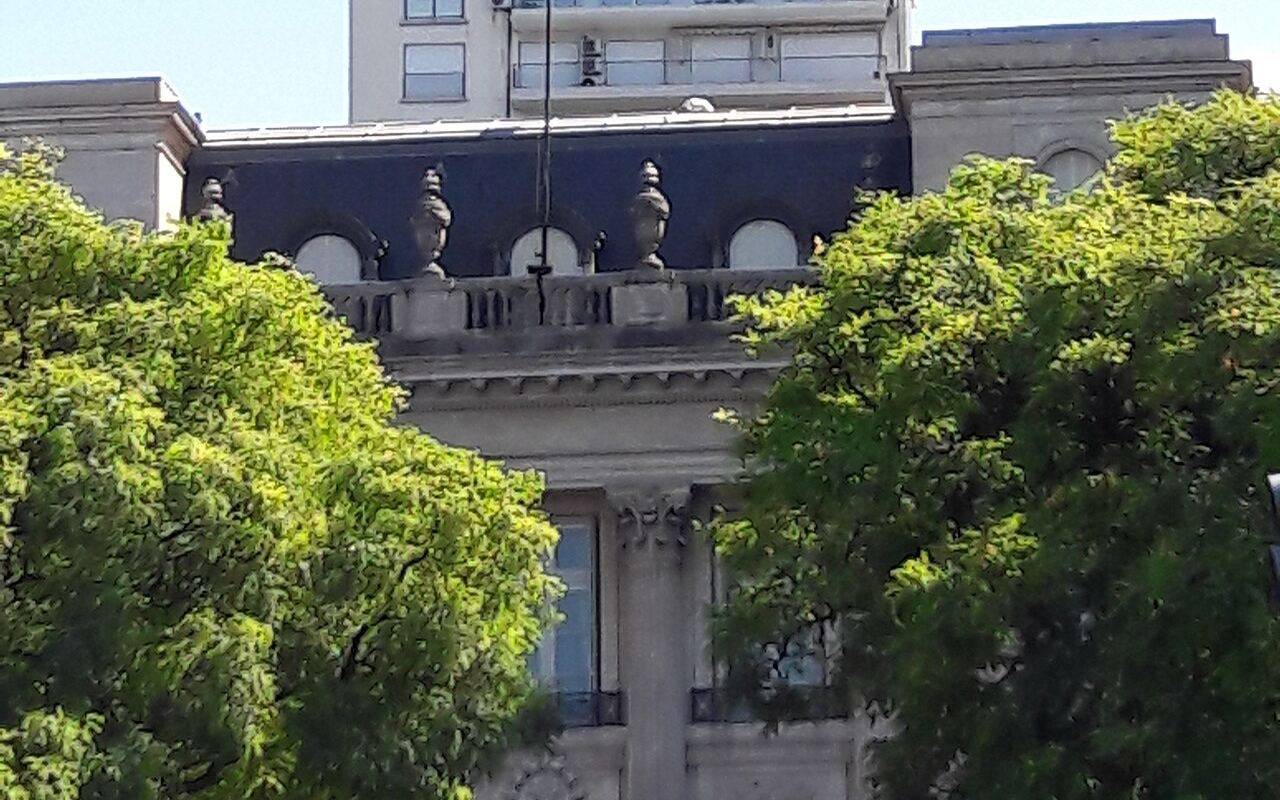 Edificio de la Embajada de Estados Unidos en Argentina, con la bandera estadounidense y árboles en primer plano.