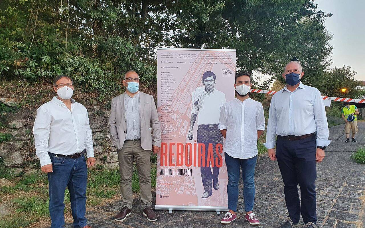 Cuatro personas de pie junto a un cartel publicitario sobre el documental de Moncho Reboiras