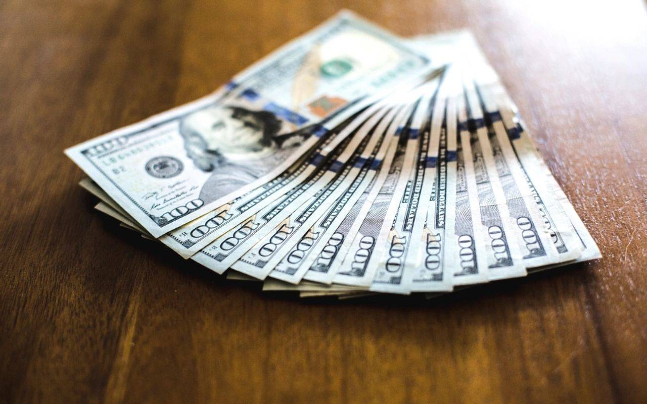 Billetes de cien dólares estadounidenses desplegados sobre una mesa de madera.
