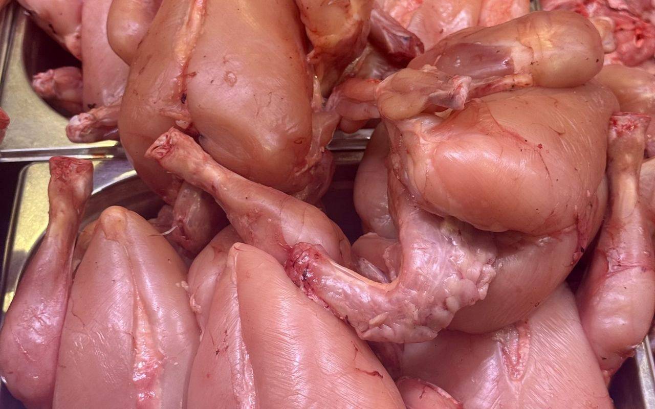 Pollos crudos desplumados, apilados en bandejas metálicas para la venta.